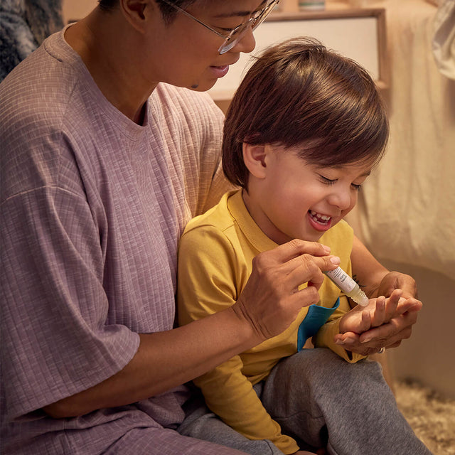 Child giggles while parent applies Aroma Fairy roll-on to child's palm